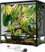 Glass reptile terrarium with green plants, branches, a chameleon, and a misting system hose