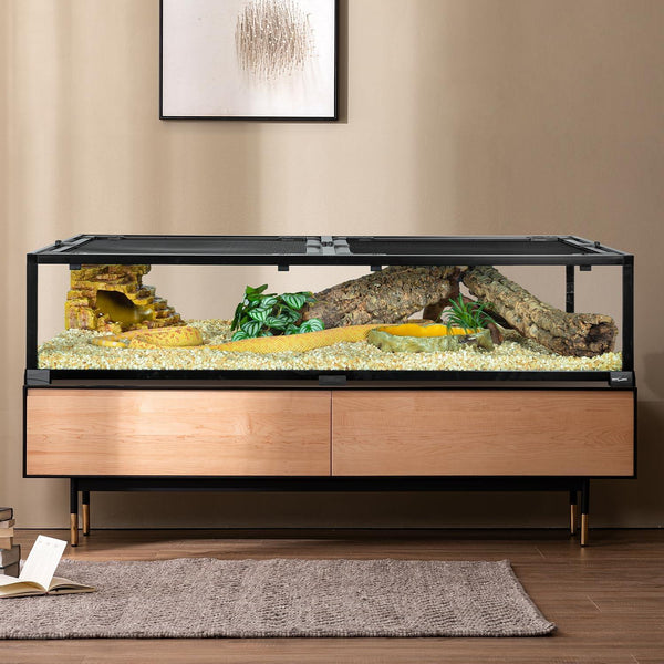 Large reptile terrarium with branches, plants, rock hide, and a yellow snake in a living room setting