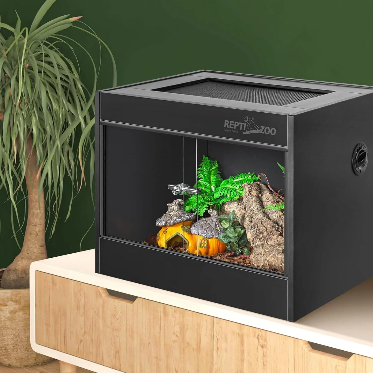 Glass reptile terrarium with sliding doors, log décor, and artificial plants on wooden cabinet