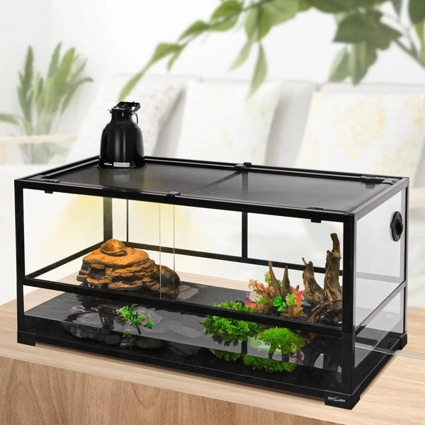 Glass reptile terrarium with mesh lid, heating lamp, rocks, and artificial plants on a table