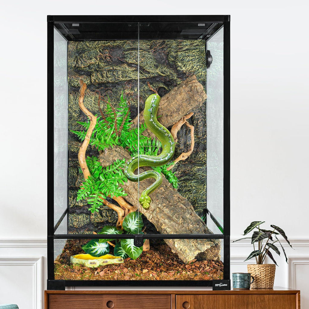 Large glass reptile terrarium with green snake, logs, branches, and lush artificial plants.