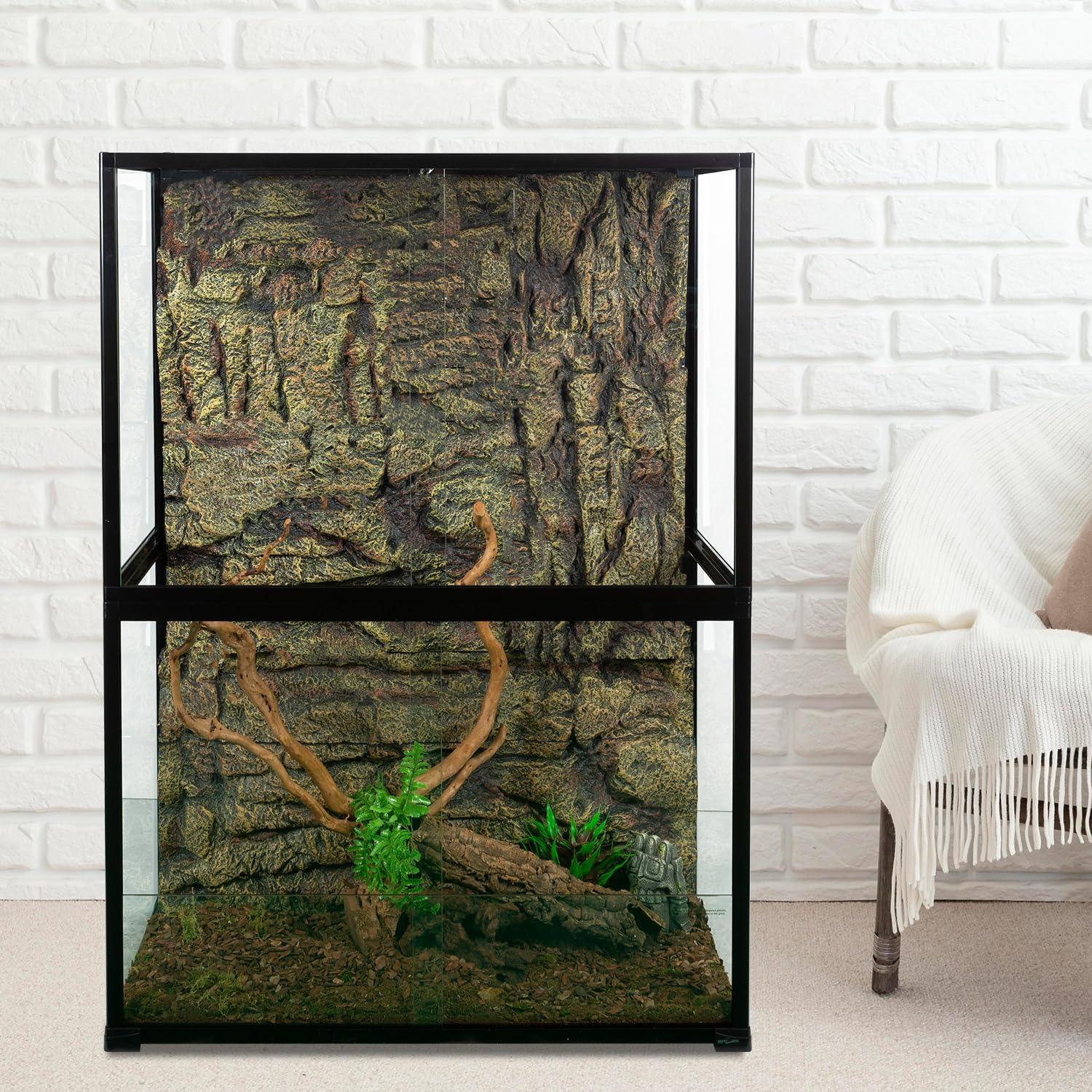 Glass reptile terrarium with rock background, wood branches, and plants against white brick wall