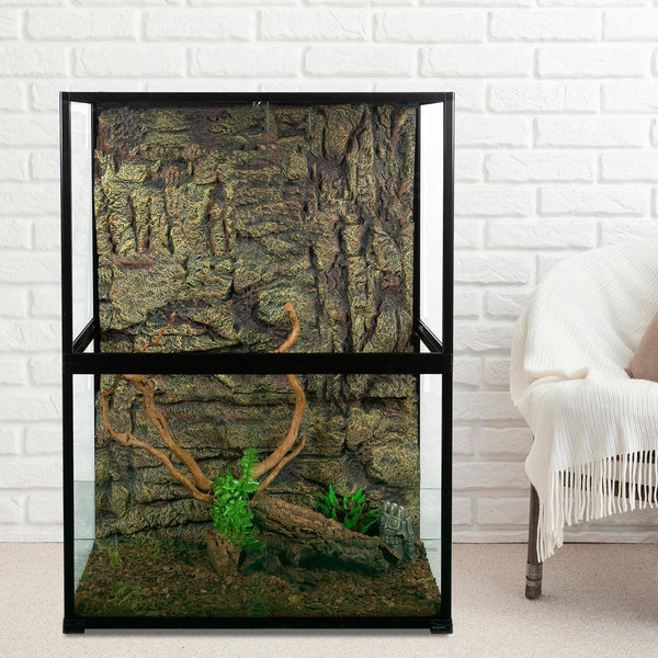 Glass reptile terrarium with rock background, wood branches, and plants against white brick wall