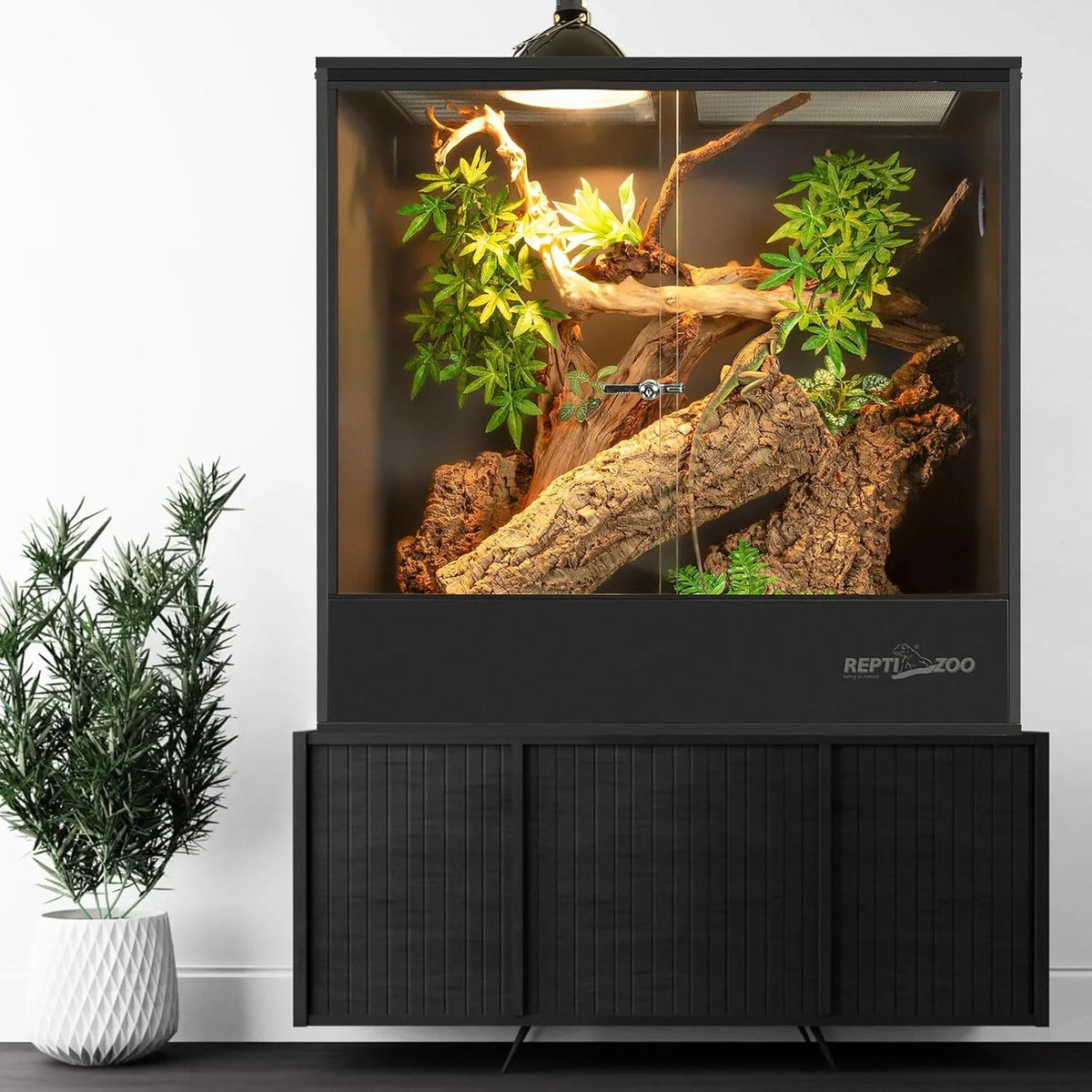 Large reptile terrarium with UVB light, branches, and artificial plants on modern cabinet