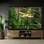 Large reptile terrarium with green snake on branch and lush tropical plants inside