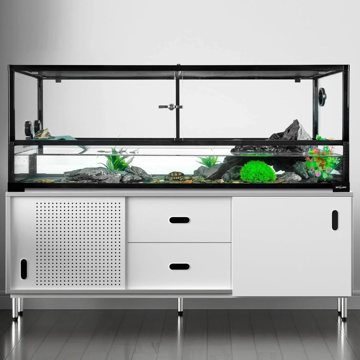 Large glass reptile terrarium with rocks, plants, and water on modern white stand.