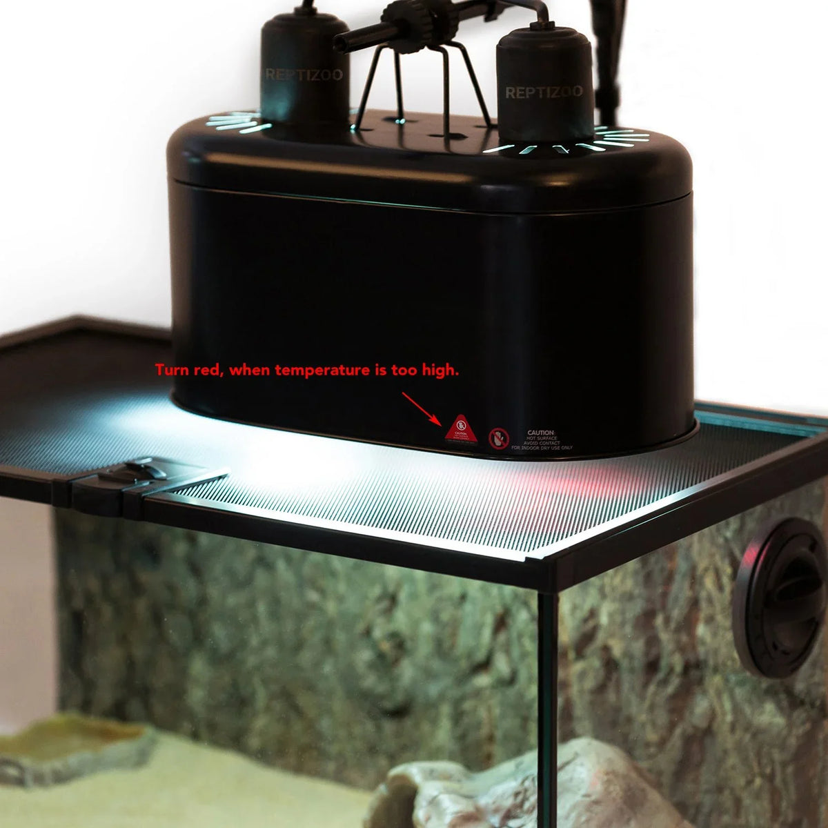 Black reptile tank heat lamp with temperature warning indicator on terrarium mesh lid.