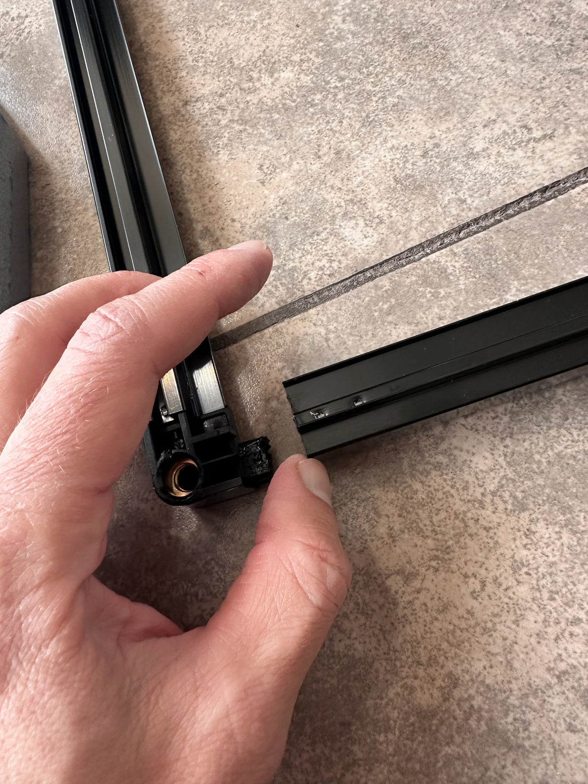 Hand assembling black aluminum frame pieces for reptile terrarium on tile surface Main image