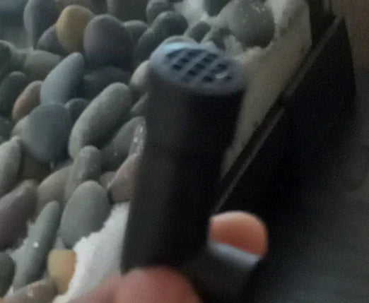 Close-up of a black terrarium misting nozzle with rocks and glass in the background Main image