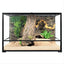 Glass reptile terrarium with naturalistic background, driftwood, plants, and sandy substrate.