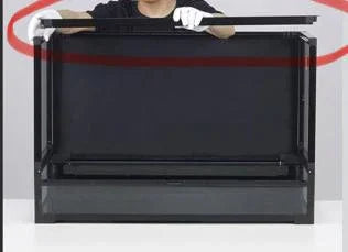 Person assembling a large black reptile terrarium enclosure on a white table